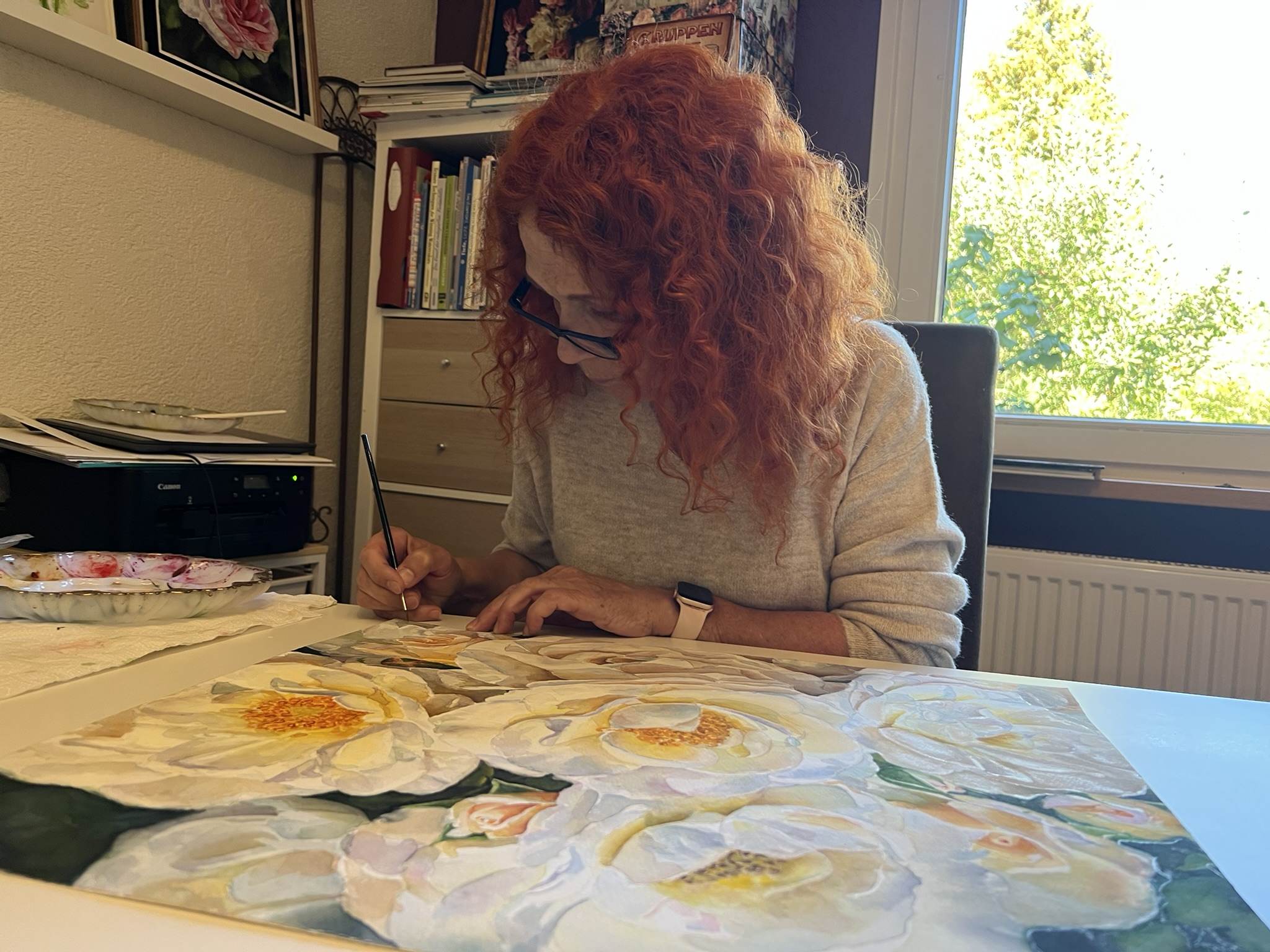 Doris Joa in a white sweater painting white roses at her studio table